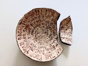 A stoneware bowl covered in writing deliberately broken into two parts to resemble a museum relic