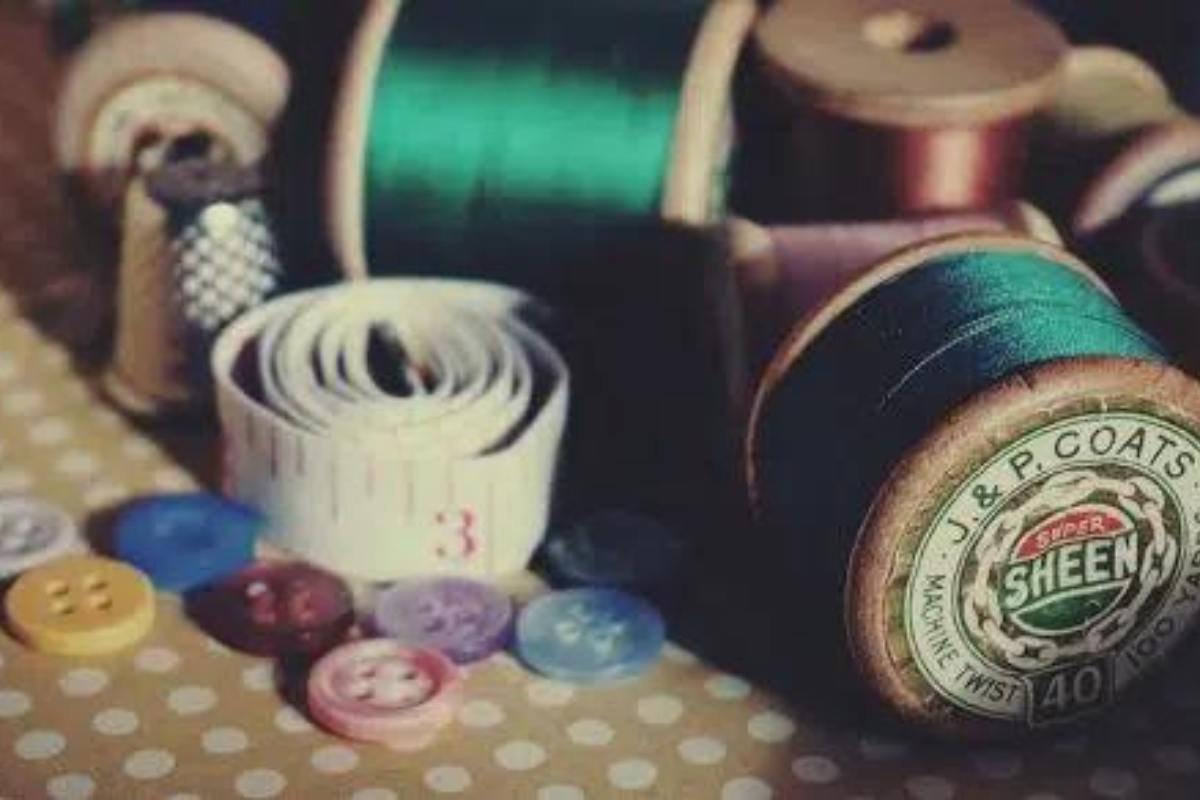 Photograph of cotton rels, a selection of buttons and a rolled up tape measure on a sewing table.
