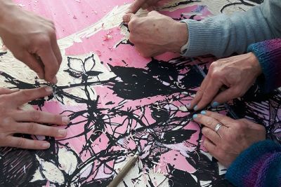 People working on a pink and black woodcut print